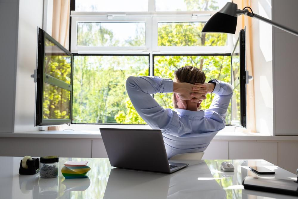 Relaxed Young Businessman Relaxing On Chair Behind Desk At Office with windows open